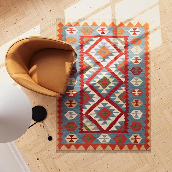 Kelim mit roten Medaillons und blauer Bordüre neben einem orangefarbenen Sessel, von oben